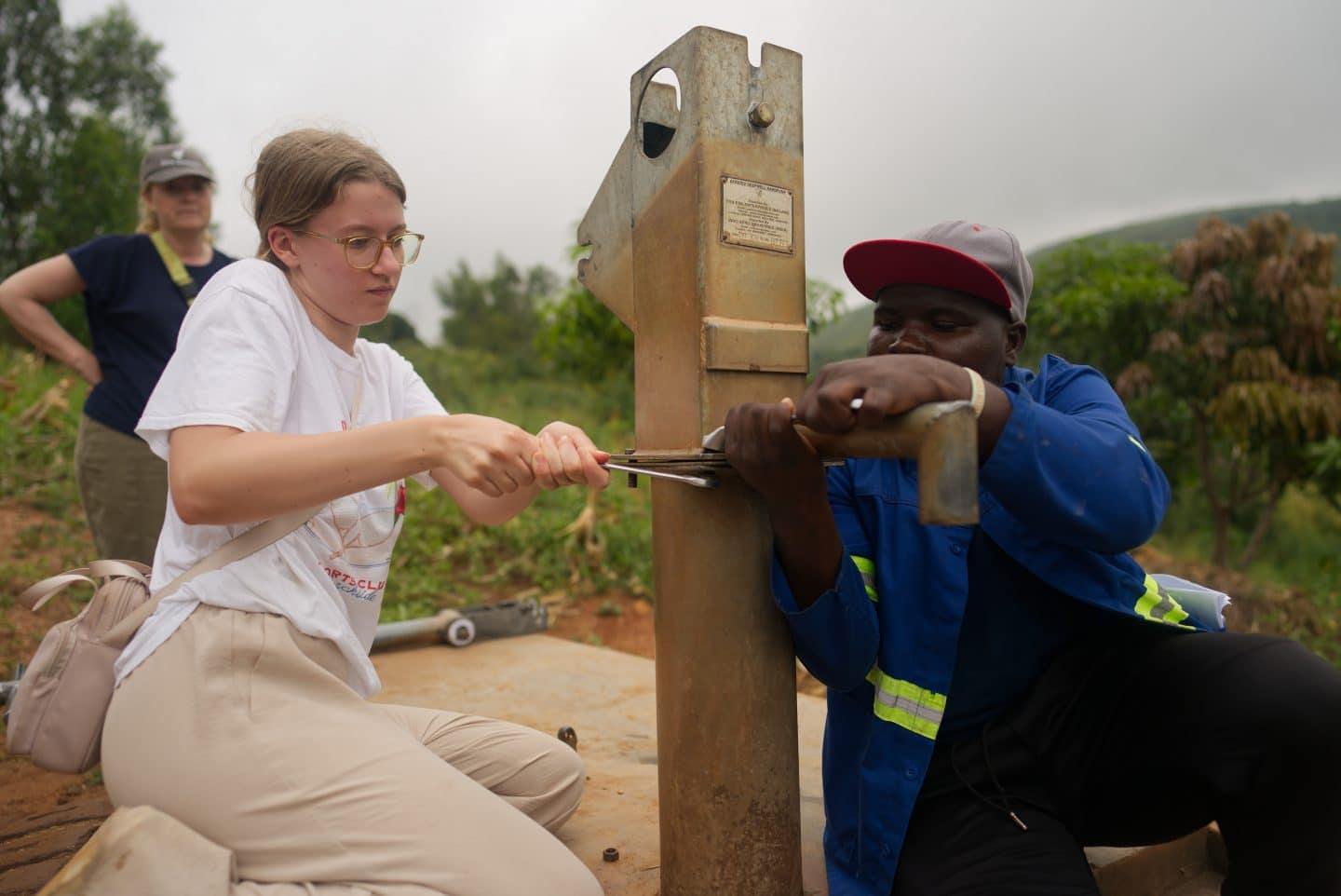 A volunteer and a member of the Madzi Alipo team are removing a bolt together from a water pump that is between them in order to take it apart to repair it