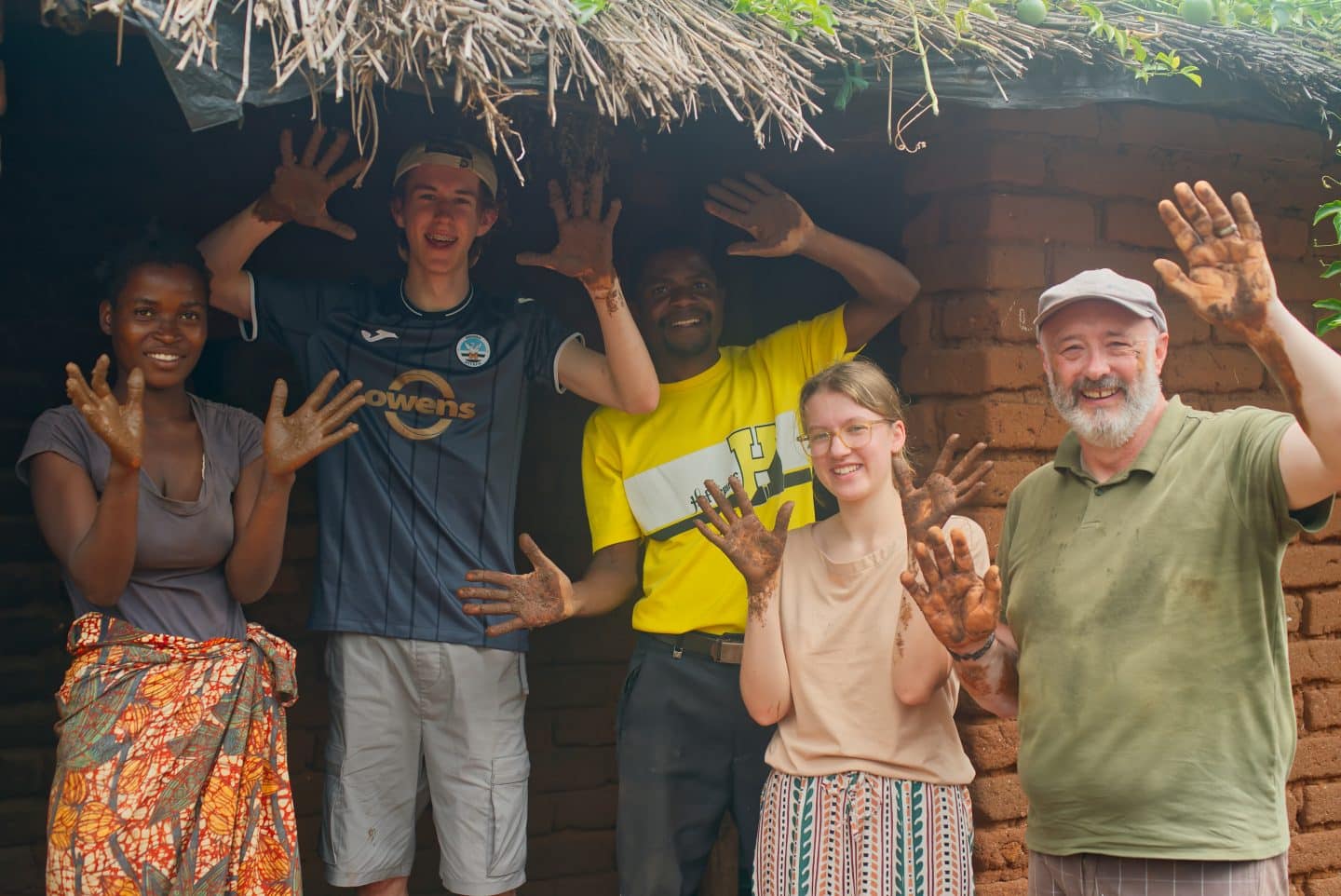 Family and guests holding up muddy hands outside a home having just finished making a fuel efficient stove.