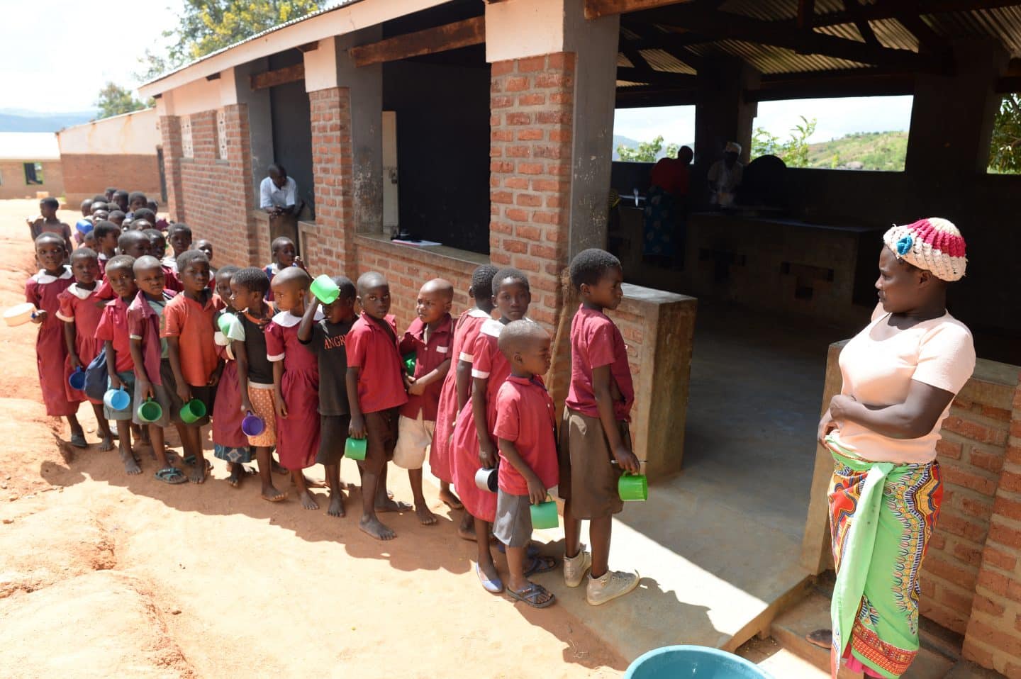 Children queuing for Phala (porridge) at Masuku School kitchen a primary school in rural Malawi supported by Fisherman's Rest community projects.